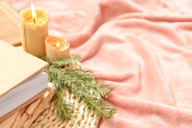 Kitapların yakın görüntüsü, köknar ağacı dalı ve yatakta yanan mumlar.