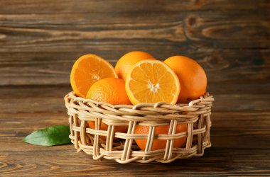 Tahta arka planda taze portakallı hasır sepet.