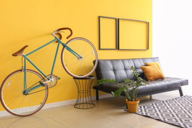 Sarı duvarın yanında bisikleti ve kanepesi olan modern bir oda.
