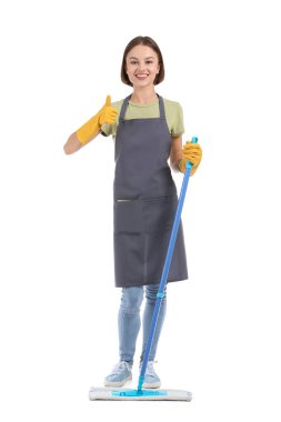 Yerleri paspaslayan güzel genç bir kadın beyaz arka planda baş parmağını gösteriyor.