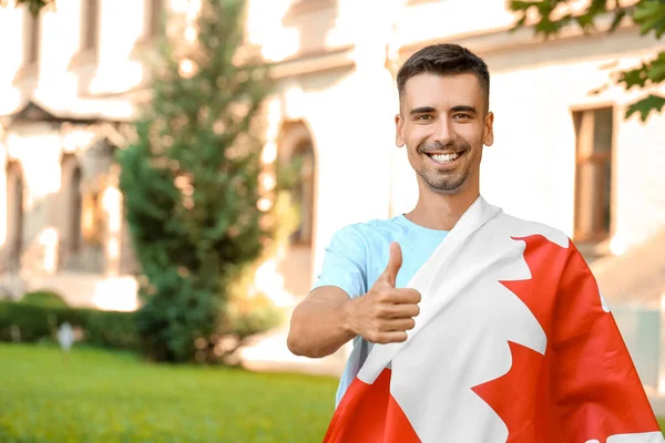 拿着加拿大国旗的年轻人在户外竖起大拇指 — 图库照片