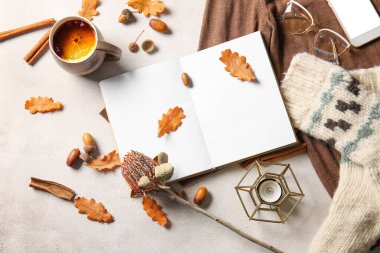 Boş kitap, bir fincan çay, cep telefonu, gözlük ve arka planda sonbahar dekoru.