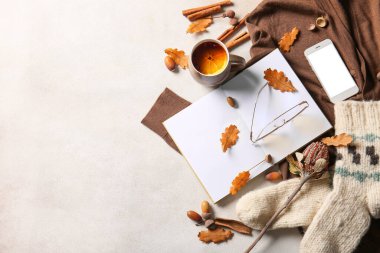 Boş kitap, bir fincan çay, cep telefonu, gözlük ve arka planda sonbahar dekoru.