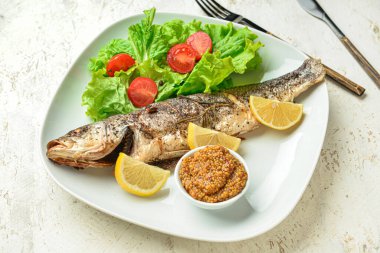 Lezzetli levrek balığı, sebze, hardal tohumlu kase ve arka planda çatal bıçak, yakın plan.