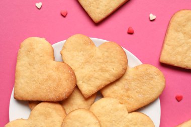 Pembe arka planda kalp şeklinde kurabiyeler olan tabak, yakın plan. Sevgililer Günü kutlaması