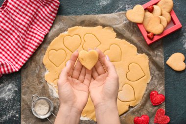 Koyu arkaplanda pişmemiş kalp şeklinde kurabiye tutan bir kadın. Sevgililer Günü kutlaması