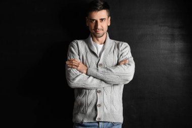 Esmer arka planda örülü süveter giyen yakışıklı bir genç.