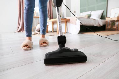 Yatak odasında elektrikli süpürgeyle ahşap kaplamaları temizleyen kadın.