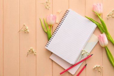 Renkli ahşap arka planda not defterleri, kalemler ve çiçeklerle kompozisyon