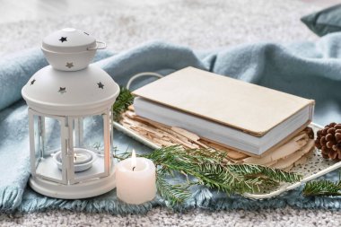 Kitaplı tepsi, fener ve ekose üzerinde yanan mum.