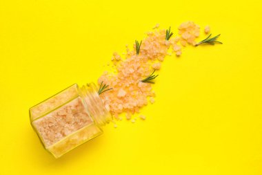 Sarı zemin üzerinde deniz tuzu ve biberiye bulunan cam kavanozla kompozisyon