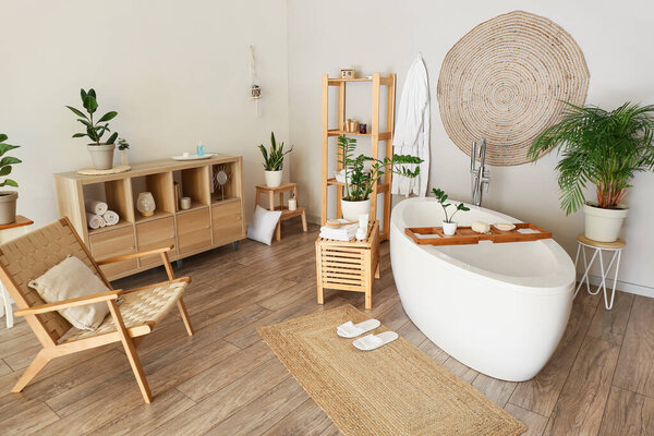 Interior of stylish bathroom with houseplants, shelving unit and armchair