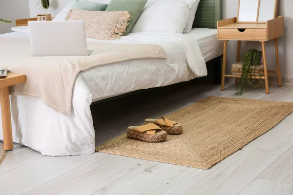 Wicker carpet with female shoes near bed in room