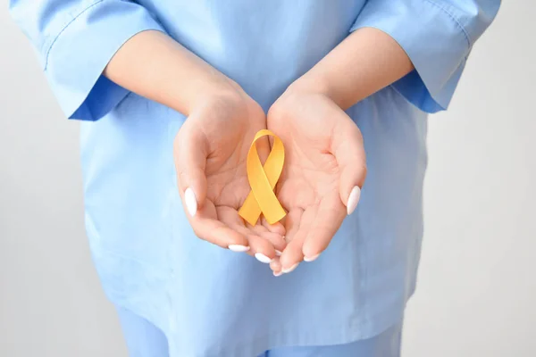 Female Nurse Holding Golden Awareness Ribbon Light Background Closeup International — Stock Photo, Image