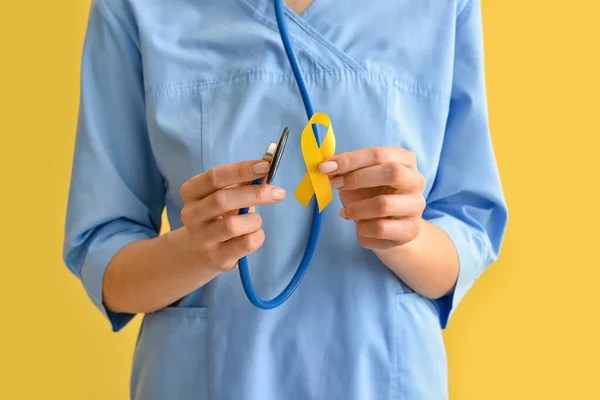 Female Nurse Holding Golden Awareness Ribbon Stethoscope Color Background International — Stock Photo, Image