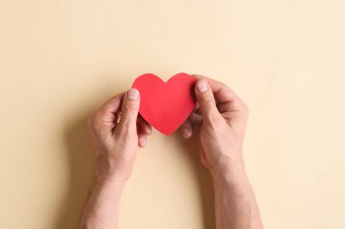 Renkli arka planda kırmızı kağıt kalp tutan adam. Bağış konsepti