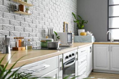 Gri tuğla duvarın yanında farklı aletleri olan modern mutfak.