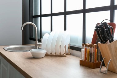 Temiz tabaklar, lavabo ve çatal bıçaklarla büyük pencerenin yanındaki ahşap masada dur.