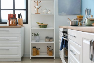 Mutfak aletleri, sepeti ve kavanozları beyaz duvarın yanında.