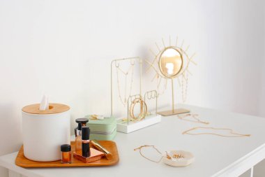 Dekoratif kozmetik ürünleri ve şık mücevherler ışık duvarının yanındaki masada.