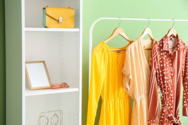 Renkli duvarın yanında şık elbiseli ve raf üniteli bir askı.