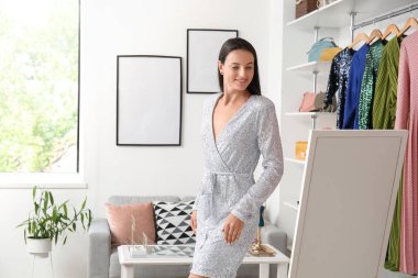 Güzel bir kadın butikte aynanın yanında şık bir elbise deniyor.