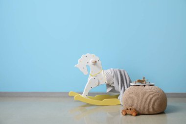 Sallanan at, ekose, puf ve renkli duvarın yanında tahta oyuncaklar.