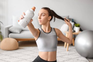 Spor kıyafetli genç bir kadın evinde bir şişe suyla, yakın plan.
