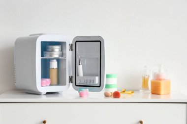 Açık kozmetik buzdolabı, açık duvarın yanındaki çekmecelerin üzerinde ürünler var.