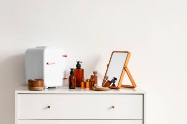 Küçük kozmetik buzdolabı, ayna ve çekmecelerde ışık duvarı yakınında bulunan ürünler.