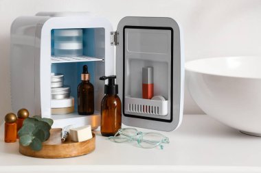 Işık duvarının yanındaki masada kozmetik ürünleri olan bir buzdolabı aç