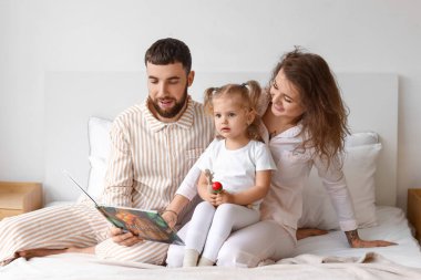Evdeki yatak odasında kitap okuyan mutlu bir aile.