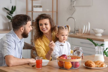 Genç ve mutlu bir aile mutfakta kahvaltı yapıyor.