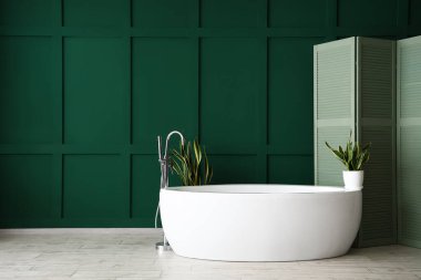 Yeşil duvarın yanında beyaz küvet ve katlanmış ekran.