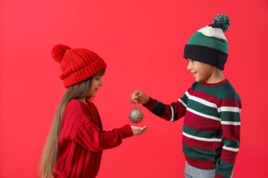 Kışlık süveter giymiş şirin çocuklar ve renkli bir Noel topu.