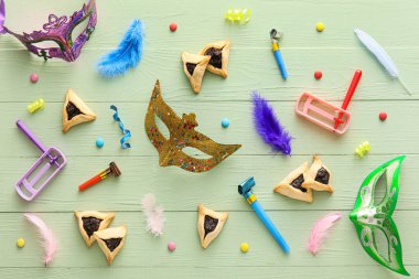 Purim bayramı için çıngıraklı çıngıraklı karnaval maskeleri ve Hamantaschen kurabiyeleri ve renkli ahşap arka planda parti üfleyicileri