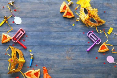 Renkli ahşap arka planda Purim bayramı için çıngıraklı karnaval maskeleri ve Hamantaschen kurabiyeleri.