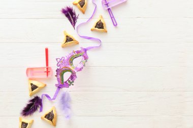 Beyaz ahşap arka planda Purim bayramı için çıngıraklı karnaval maskesi ve Hamantaschen kurabiyeleri