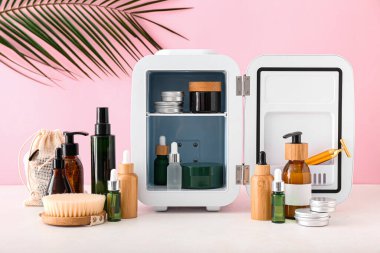 Kozmetik ürünleri ve ışık masasında tropikal yapraklı küçük buzdolabı.