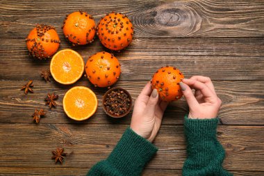 Ahşap arka planda karanfilli mandalinadan yapılmış el yapımı Noel süsü yapan kadın.