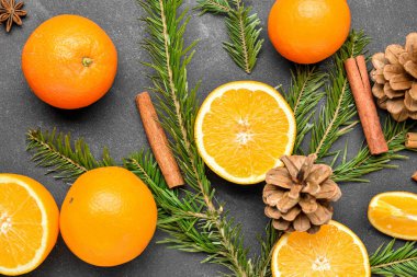 Taze portakallar, köknar dalları ve siyah arkaplanda çam kozalakları.