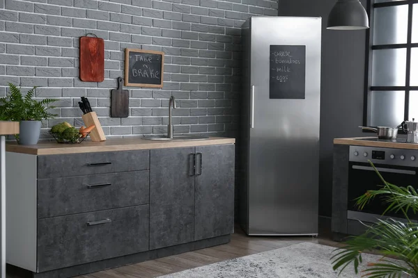 Fridge with list of products and stylish furniture in modern kitchen