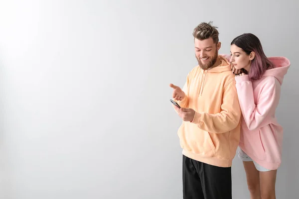 Cool Pareja Joven Sudaderas Con Capucha Con Teléfono Sobre Fondo — Foto de Stock