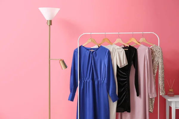 Floor lamp and hanger with elegant dresses near color wall