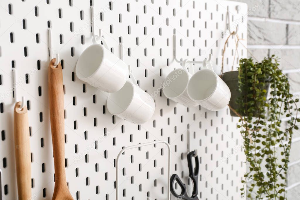 Pegboard with cups and kitchen utensils on wall