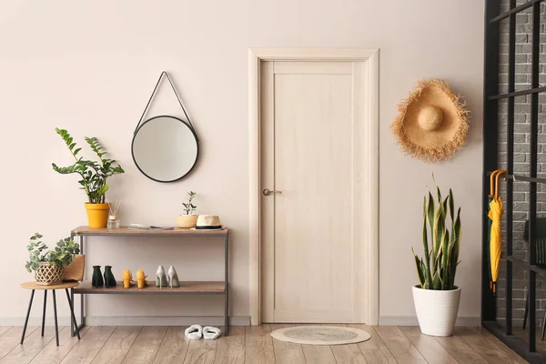 Interior of hallway with stand for shoes, mirror and houseplants near light wall