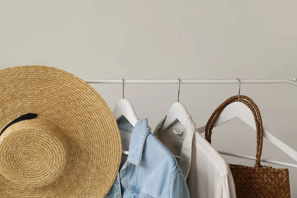 Rack with female clothes, hat and bag near light wall, closeup