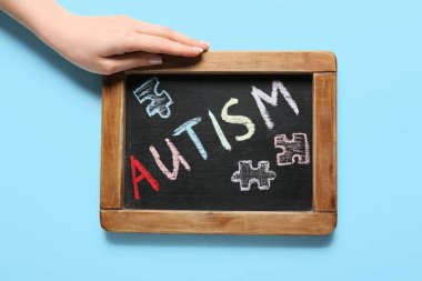 Renk arkaplanına karşı tahtaya AUTISM sözcüğüyle kadın eli