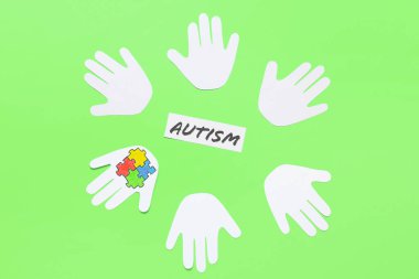 Renkli yapboz parçalarına ve renk arkaplanına AUTISM sözcüğüne sahip kağıt insan avuç içleri