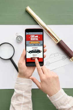 Yeşil ahşap arka planda açık araba kirası uygulaması olan cep telefonu kullanan kadın